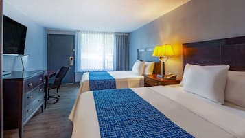 A hotel room with two beds, a desk, a chair, a TV, and a window with curtains.