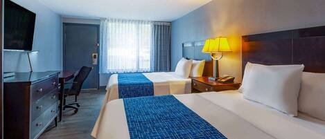 Quarto de hotel com duas camas, uma mesa, uma cadeira, televisão e janela com cortinas.
