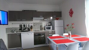 Une cuisine moderne équipée d’un lave-vaisselle, d’un four à micro-ondes et d’une cuisinière. On y trouve une table à manger avec des sets de table rouges et un vase rempli de fleurs.