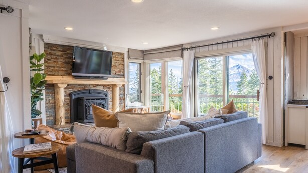 A modern living room with a large grey sectional sofa, a fireplace, and a TV mounted on a brick wall.