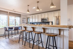 Una cucina moderna con mobili bianchi, un frigorifero in acciaio inossidabile, un'isola in legno con sgabelli da bar e illuminazione a sospensione.