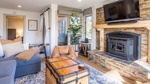 A cozy living room with a fireplace, a television mounted above it, and a large window with curtains.
