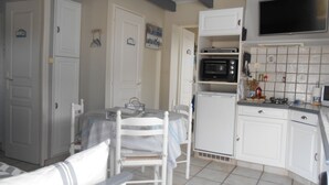 Une cuisine compacte avec des meubles blancs, un four à micro-ondes, un petit réfrigérateur et un coin repas comprenant une table et des chaises.