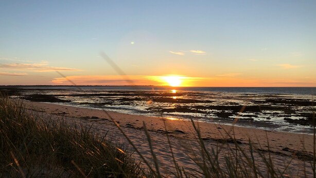 Une plage où le soleil se couche à l’horizon, créant une silhouette du paysage.