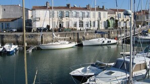 Un port de plaisance où sont amarrés plusieurs bateaux, un mur de pierre et une rangée de bâtiments au style architectural traditionnel.