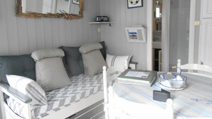 Une pièce chaleureuse avec un canapé, une table sur laquelle se trouve un livre et un panier, et une porte qui donne sur une autre pièce.