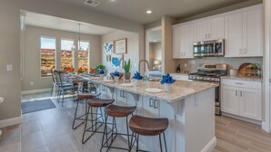 Une cuisine moderne avec des meubles blancs, un grand îlot central doté de tabourets de bar, des appareils en acier inoxydable et une vue sur un paysage désertique grâce à de grandes fenêtres.