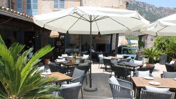Ein Straßencafé mit Tischen, Stühlen, Sonnenschirmen und Blumentöpfen.