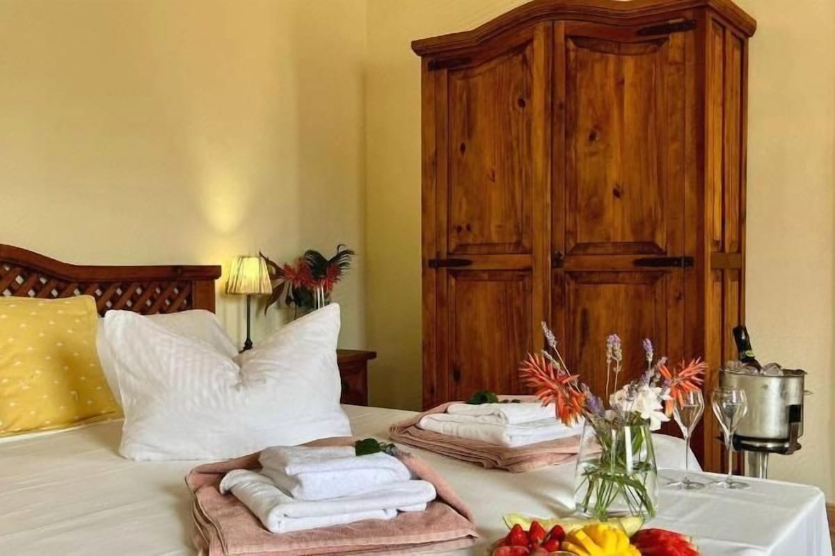 Ein Hotelzimmer mit einem Bett, einem Holzschrank, einem Tisch mit Handtüchern und Blumen sowie einer Lampe.