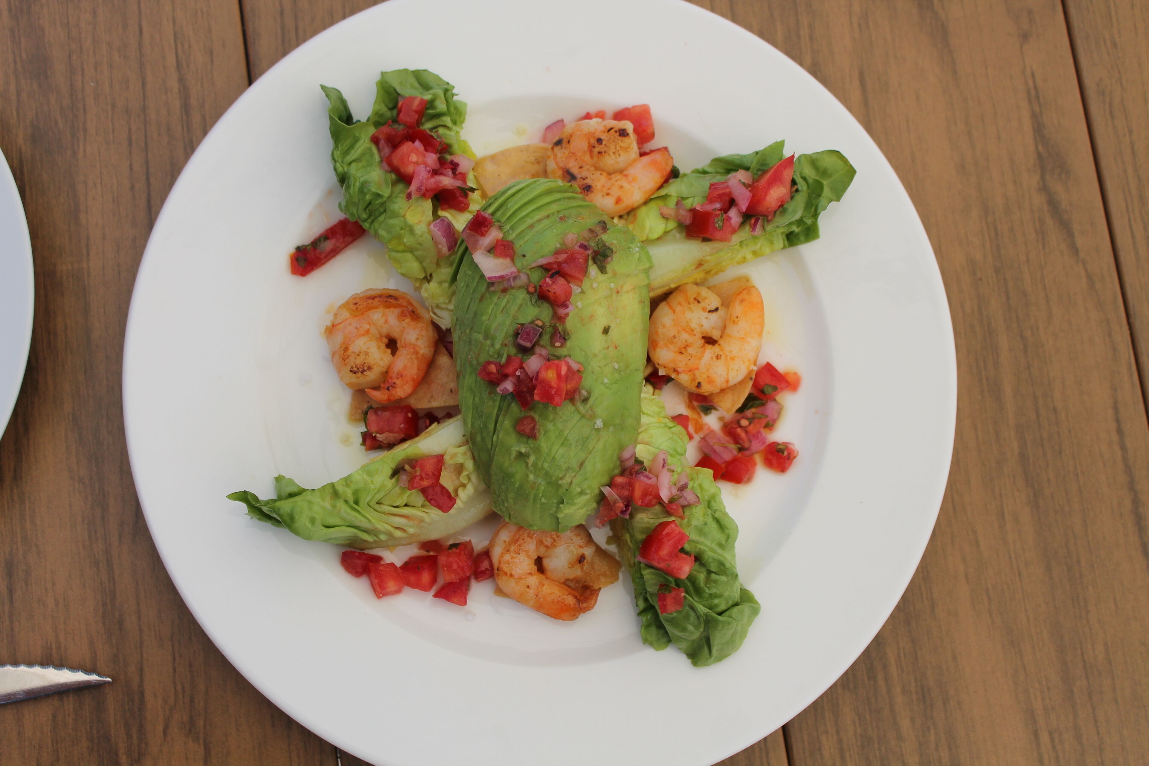 A plate of shrimp and avocado salad on a wooden table.