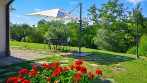 Un patio con una mesa, sillas, un paraguas blanco y flores rojas.
