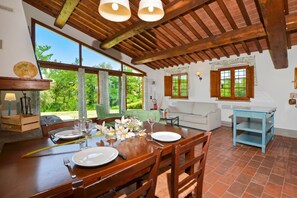 Un comedor con una mesa de madera preparada para dos personas, un sofá y una ventana con vistas a la vegetación.