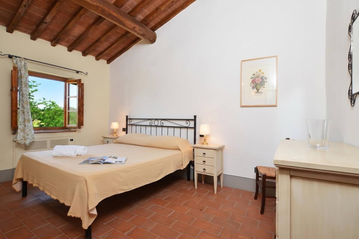 A bedroom with a bed, bedside tables, a desk, and a window with a view.