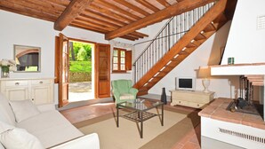 Una sala de estar con un sofá, una mesa de centro de vidrio, un sillón verde, una chimenea, un televisor y una escalera.