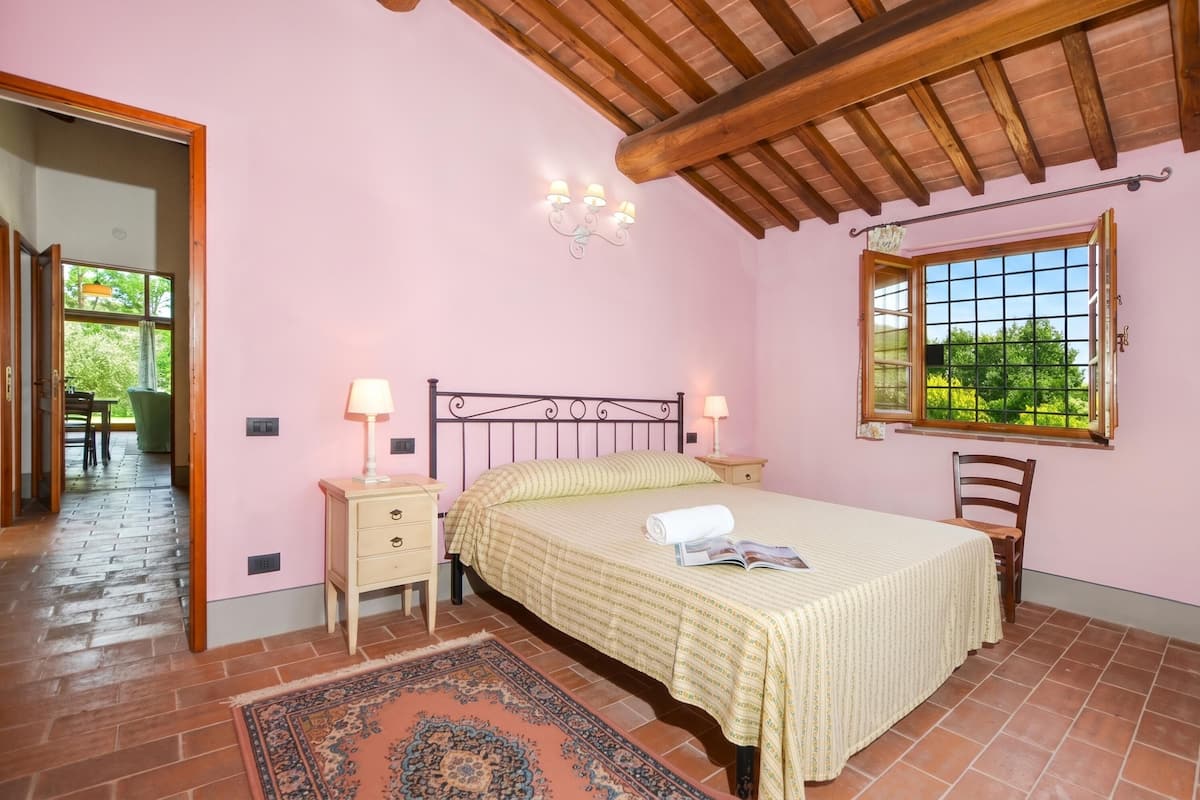A bedroom with a bed, bedside tables, a window, and a view of greenery.