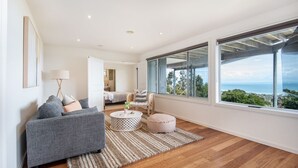 A modern living room with a grey sofa, a round coffee table, and a view of the ocean through large windows. - Pet Friendly - Cook's Lookout McCrae (McCrae)