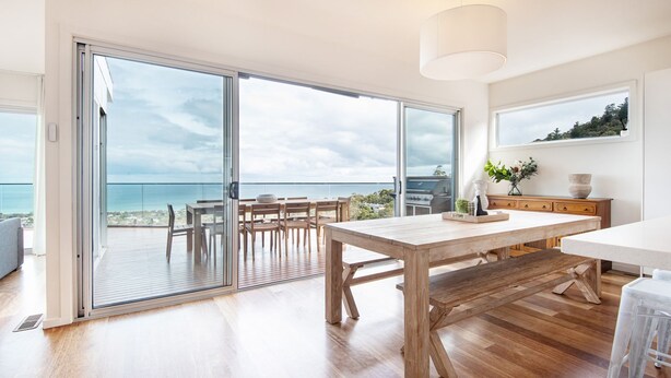 A spacious room with a wooden dining table, a kitchen area, and large sliding glass doors leading to a balcony with a view of the ocean. - Pet Friendly - Cook's Lookout McCrae (McCrae)