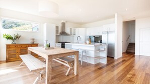 A modern kitchen with white cabinetry, a wooden dining table, and a built-in island with bar stools. - Pet Friendly - Cook's Lookout McCrae (McCrae)