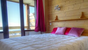 Una cama en una habitación con paneles de madera, un ventanal con vistas y un estante con dos objetos decorativos.