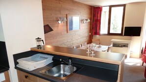 Cocina compacta con lavamanos, cafetera y comedor con mesa y sillas.