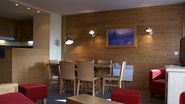 Una habitación con paredes de madera, una mesa de comedor con sillas, un sofá rojo y un cuadro.