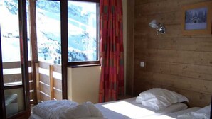 Una habitación con una cama, un ventanal con vistas a un paisaje nevado y una pared de madera.