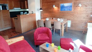 Una sala de estar acogedora con sofás rojos, una mesa de comedor de madera y una zona de cocina con armarios de madera.
