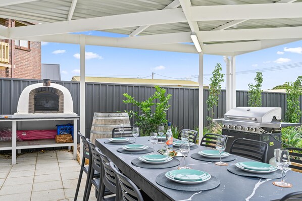 Eine Terrasse im Freien mit einem langen Esstisch, einem Pizzaofen und einem Grill.