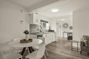 A modern kitchen with white cabinets, a dining area with a white table and chairs, and a small seating area with a sofa and a side table. - The HardyOne ~ Aldinga Beach - Stunning Abode in Serene Silver Sands (Aldinga Beach)