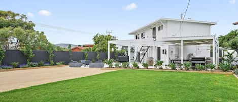 Ein modernes, zweistöckiges Haus mit überdachter Terrasse, sichtbarer Treppe und gepflegtem Rasen.