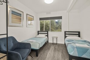 Une chambre avec deux lits simples, une chaise et une fenêtre donnant sur des arbres.