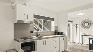 Uma cozinha moderna com armários brancos, forno embutido, bancada de aço inoxidável e uma janela com vista para o verde.