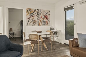 Un salon moderne avec un coin repas, agrémenté d’un grand tableau abstrait, d’un canapé en cuir marron et d’une vue sur l’extérieur grâce à une porte vitrée.
