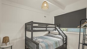 Uma cama beliche com janela, uma mesinha e um candeeiro suspenso.