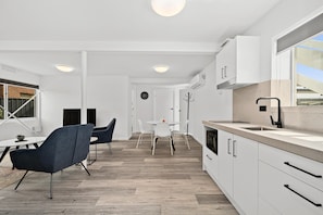 Une cuisine moderne avec des meubles blancs, une grande fenêtre et un coin repas comprenant une table ronde et des chaises.