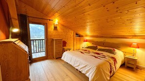 Camera da letto in accogliente baita di legno, con un letto grande, una cassettiera e una finestra vista foresta.
