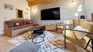 Un accogliente soggiorno con soffitto in legno, parete in pietra, televisore a schermo piatto, divano con cuscini, tavolino da caffè e una poltrona.