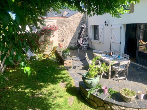 A stone patio with a table and chairs, surrounded by potted plants and a wooden fence. - Charming Renovated House with Garden in the Heart of Salt Marshes, Close to Guérande and La Baule (Guérande)