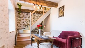 A cozy living room with a wooden table, a red sofa, and a staircase leading to a loft area. - Charming Renovated House with Garden in the Heart of Salt Marshes, Close to Guérande and La Baule (Guérande)
