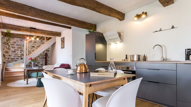 A modern kitchen with a wooden table, white chairs, and a built-in stove. - Charming Renovated House with Garden in the Heart of Salt Marshes, Close to Guérande and La Baule (Guérande)