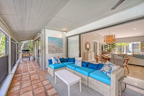 Open living and dining area with sofa, ceiling fan, terracotta tile flooring, and tropical views