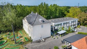 Ein großes Gebäude mit weißer Fassade und grauem Dach, neben einem Golfplatz mit grünen Spielbahnen und Sandbunkern.