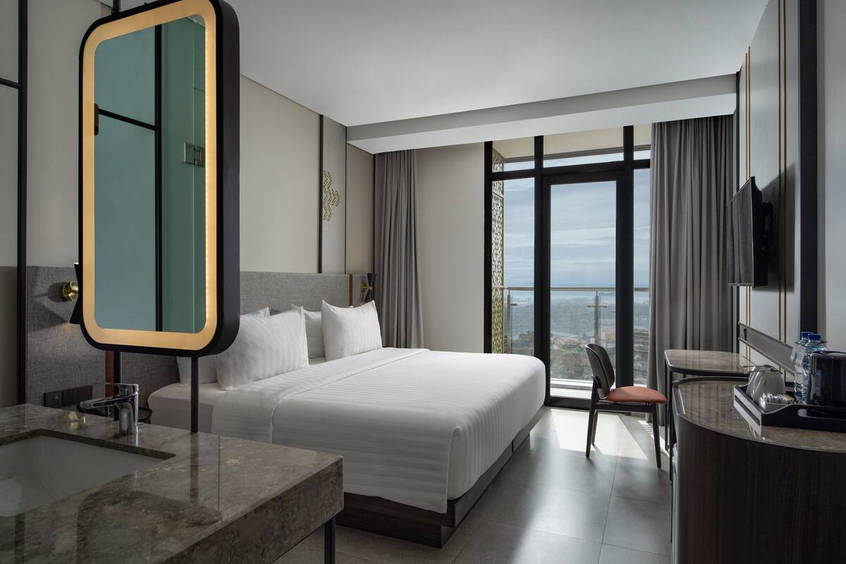Una habitación de hotel moderna con una cama grande, un baño con espejo, un escritorio y vistas a la ciudad.