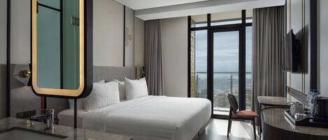 A modern hotel room with a large bed, a bathroom with a mirror, a desk, and a view of the city.