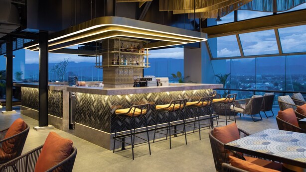 A modern bar area with a high bar and seating, overlooking a cityscape. - Hotel Santika Premiere Padang (Padang)