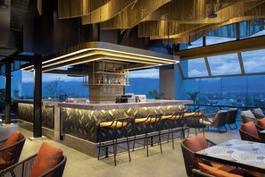 A modern bar area with a high bar and seating, overlooking a cityscape. - Hotel Santika Premiere Padang (Padang)