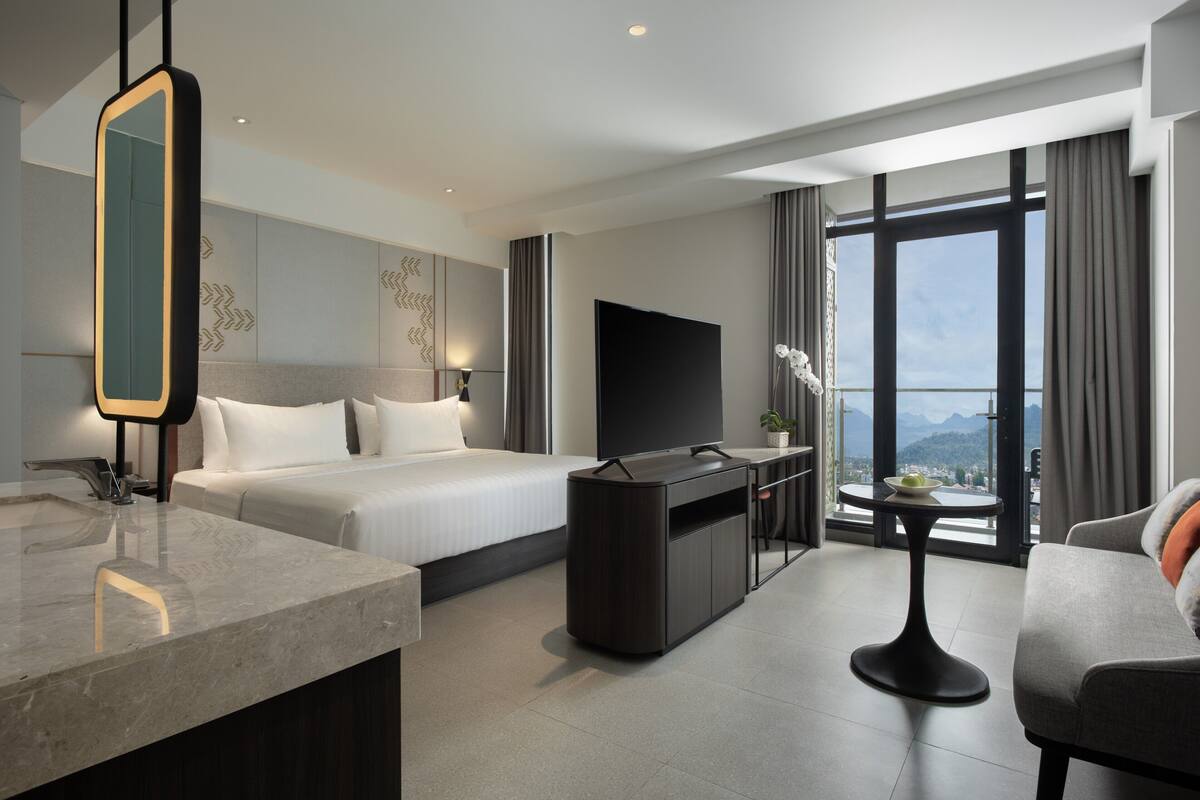 Habitación de hotel moderna con cama, televisión, escritorio y vista a las montañas.