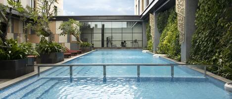 Una piscina con suelo de baldosas, rodeada de plantas en macetas y bancos.