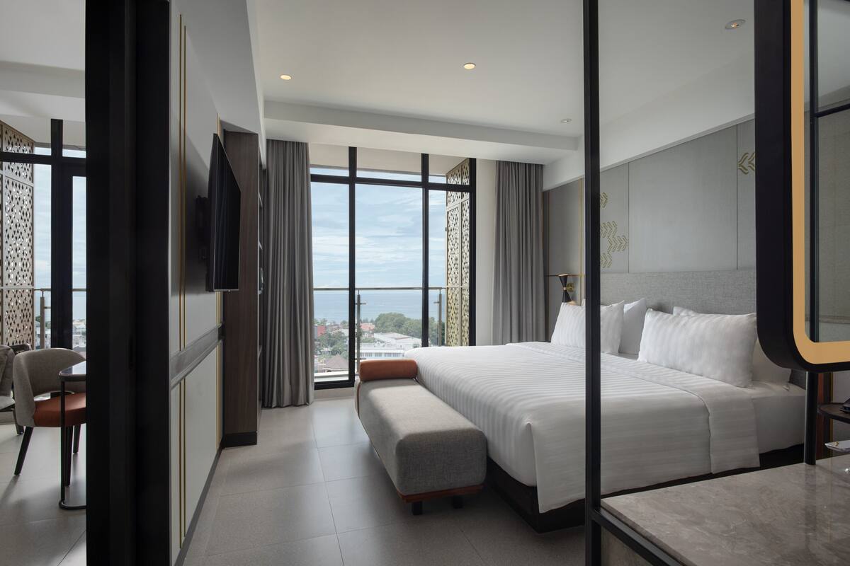 Una habitación de hotel moderna con una cama grande, un área de descanso, televisión y vistas a la ciudad.