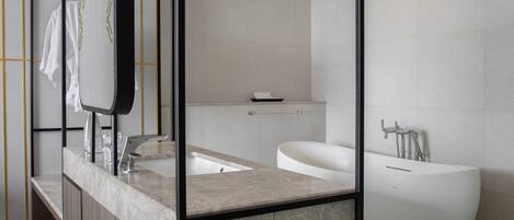 Un baño moderno con una bañera grande, un lavamanos independiente y un espejo. Hay repisas con toallas y pantuflas.